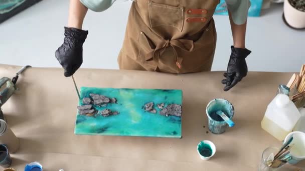 女性アーティストはエポキシ樹脂を吸収し 木製板にスティックで塗ります 液体アート技術を用いた熟練した職人技 海と波の写真を作成し 岩の上の景色を眺める 樹脂アートのマスタークラス — ストック動画