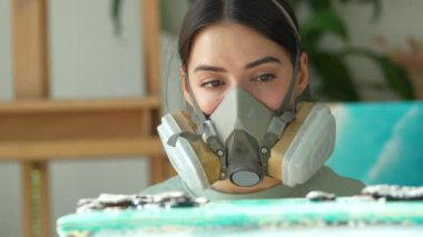 Konsantre İspanyol kadın ressam solunum maskesi takıyor. Epoksi reçinesi döktükten sonra tabloyu inceliyor. Çalışma kalitesini kontrol ediyor. Reçine sanatı, el yapımı zanaat. 