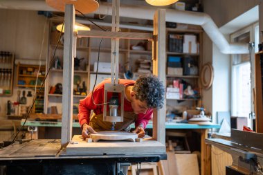 Professional man carpenter works with joinery equipment. Careful attentive craftsman master in workshop engaged in installation of wooden block board on machine before processing. Small DIY business. clipart