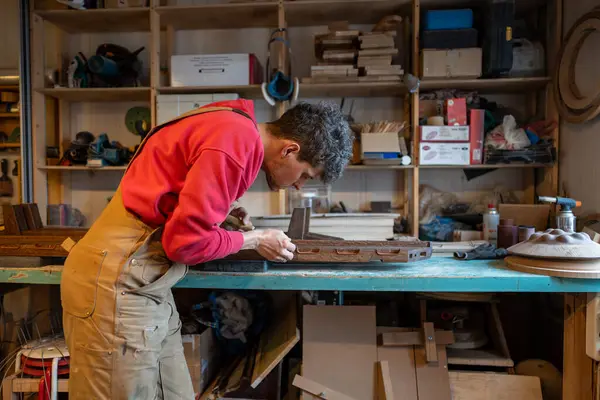 stock image Concentrated man carpenter use chisel to wooden handmade product in joinery workshop. Focused master guy carefully makes DIY slatted base to bed. Small business craftsmanship skill attention to detail