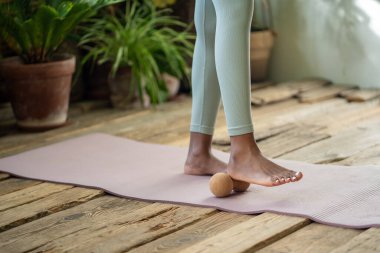 Yoga minderinde bacaklar yuvarlanan fitness topu. Siyahi kadın özbakımı, miyofasyal masaj topu, yuvarlanan ayak, gevşeme ve kan dolaşımını iyileştirme ile çalışır. Sağlıklı yaşam tarzı için spor aletleri.