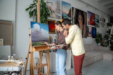 Sanat stüdyosunda resim çizen yaratıcı kadın ressam, kocası süreçten ve iyi ilişkiden hoşlanıyor. Sevgi dolu erkek destekçisi kadın ressam tablo çiziyor resim atölyesinde ayakta duran tablolar.