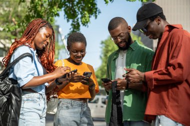 Afro-Amerikan genç öğrencilerden oluşan akıllı telefonlardan oluşan bir grup açık havada birbirleriyle iletişim kurmadan sosyal medyaya göz gezdiriyorlar. Telefon bağımlılığıyla ilgilenen arkadaşlar.