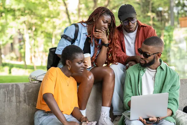 stock image Concentrated on education group of African American students look at laptop screen discusses class project or study for test sits outside university campus. Interested black young friends near college