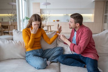 Nervous aggressive emotional husband threatening helpless unhappy wife. Stressed female crying, closing face with hand. Conflict, harassment, crisis, arguing, home violence, jealousy in family life clipart