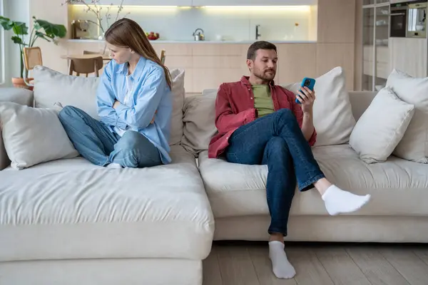 stock image Upset sad woman offendedly turned away from enthusiastic husband with mobile phone, not paying attention to resentful wife. Melancholy female feels lonely with man who ignoring talk looking on screen.
