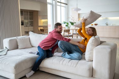 Neşeli koca, hassas ve mutlu eşi gıdıklıyor. Modern dairede kanepede yastıklı bir adamla kavga eden gülen kadın. Mutlu sevgi dolu aile eğleniyor, seviniyor, mutlu oluyor, mutlu oluyor.