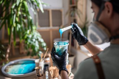 Odaklanmış kadın sanatçı epoksi reçinesini karıştırıyor sıvıyı karıştırıyor ve plastik bardakta boyayla boyuyor. Kalınlığı ve gerekli tutarlılığı değerlendiren konsantre bir kadın işe başlamadan önce.
