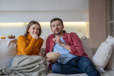 Şaşırmış aile çifti TV şovu, film, diziler evde kanepede oturup patlamış mısır yiyor. Harika, rahat, evli bir adam ve kadın heyecan verici bir hikayeyle birlikte eğleniyorlar.