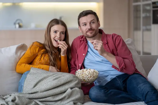 stock image Smiling woman, satisfied man relaxing, spending fun time together, snacking. Peaceful husband boyfriend, joyful girlfriend wife sitting on sofa, enjoying interesting comedy film on television. 