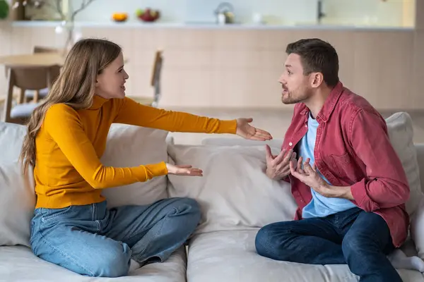 stock image Married couple spouses quarrel, squabbling, fighting, vigorously gesticulating while sitting on couch. Aggressive wife blaming husband making excuses. Guy and girl violently discussing acute issue.