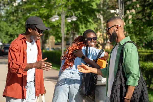 Afro-Amerikan dostlarımızın keyifli bir selamı var. Neşeli siyah öğrencilerden oluşan mutlu bir grup birlikte vakit geçirmek için birbirlerine sarılıyorlar. İki erkek tokalaşıyor, kızlar gülümsüyor, birbirlerini görüyorlar.