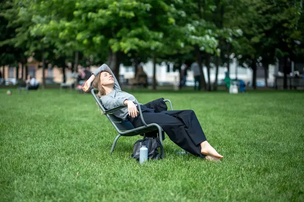 stock image Relaxed lazy sleepy woman lounges in lounger chair in green public park on hot summer day. Siesta, laziness, and inability to work in hot weather. Female rests in the park on weekends or vacation