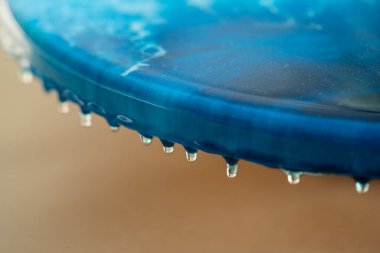 Closeup of blue epoxy resin drying on canvas, droplets flowing from edge of artwork. Resin texture forms glossy surface as it solidifies, macro fluid motion. Craftsmanship, design, creativity clipart