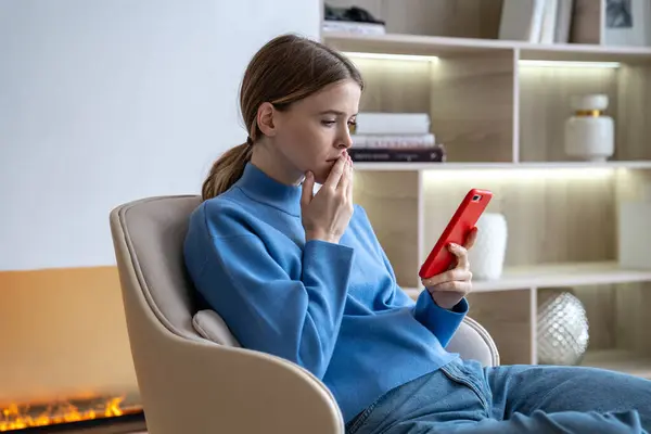 stock image Shocked gloomy woman receives bad news on smartphone. Upset female sitting in armchair reading message in depression, crisis. Work problems, relationship difficulties, chat on phone, scrolling feed