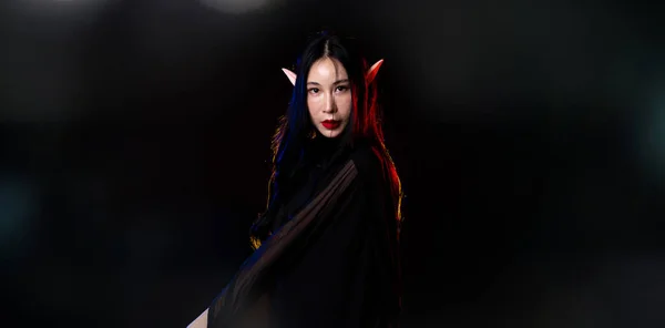 黒ファンタジーロープの長いドレスキャスト呪文魔女の周りを流れる妖精の女性の自己女王 美しい顔をしたプリンセスガール鋭い耳 古いスタイルの洞窟 闇の魔法を黒の背景に吹き飛ばせ — ストック写真