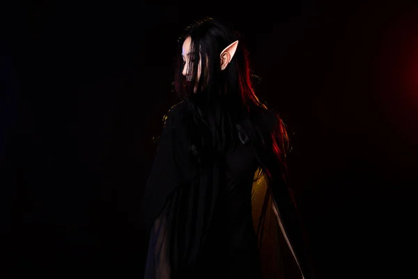黒ファンタジーロープの長いドレスキャスト呪文魔女の周りを流れる妖精の女性の自己女王 美しい顔をしたプリンセスガール鋭い耳 古いスタイルの洞窟 闇の魔法を黒の背景に吹き飛ばせ — ストック写真