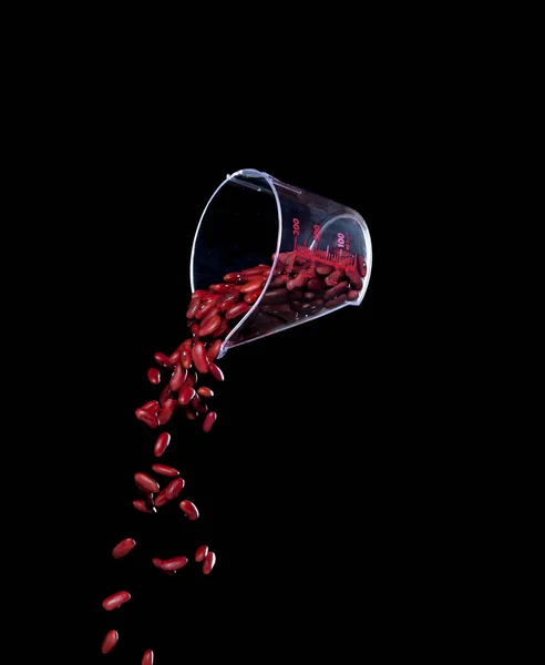 Red Bean fall, red grain beans explode abstract cloud fly from measuring cup. Beautiful complete seed pea bean, food object design. Selective focus freeze shot black background isolated