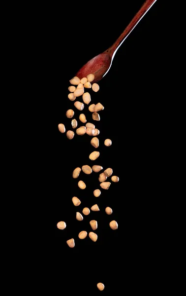 花生酱落下来 褐色的谷物花生从木勺里喷出抽象的云彩 漂亮完整的豌豆籽花生 食物物体的设计 选择性聚焦冻结拍摄黑色背景隔离 — 图库照片