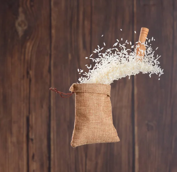 Japanese Rice in sack bag flying explosion, white grain rices fall abstract fly. Beautiful complete seed rice bag splash in air, food object design. Wood kitchen background, high speed freeze motion