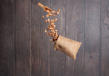 Peanut flying in sack bag, brown grain peanuts throw abstract float. Beautiful complete seed pea peanut sack bag splash in air, food object design. Wooden background high speed shutter freeze shot