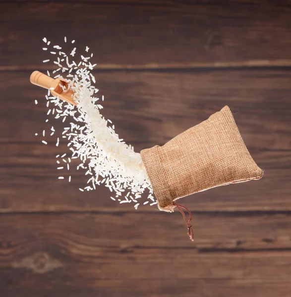 Japanese Rice in sack bag flying explosion, white grain rices fall abstract fly. Beautiful complete seed rice bag splash in air, food object design. Wood kitchen background, high speed freeze motion