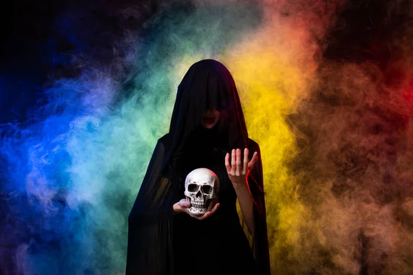 Old Witch costume woman craft spell horror magic on Horror night with Evil makeup face Art scary Magician smoke skull death hands. Colorful fog smoke over black background copy space