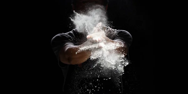 シェフはベーカリー食品を調理するための白い小麦粉のほこりを準備します 高齢者のシェフ拍手手 白い小麦粉のほこり空気中で飛ぶ爆発 フローストップモーション空気中で凍結高速シャッター 黒の背景 — ストック写真
