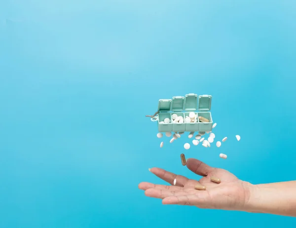 Daily pill drug medicine box container falling down to patient hand. Many kind of drugs pills medicines to help patient fly to senior hand. Drug pill Medical over blue background isolated