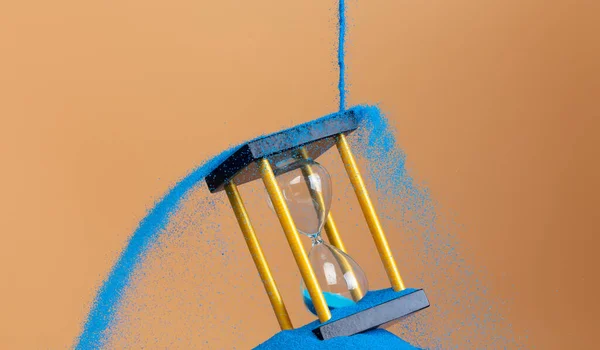 沙漏是金钱的时间沙漏 企业将蓝色沙漏倒入沙漏中 增加了更多的财务时间 截止日期将时间管理的理念延伸到黄金小时玻璃 橙色背景日落 — 图库照片