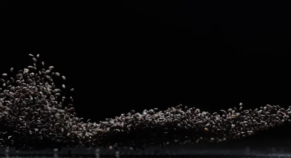 Black Sesame seeds flying explosion, black grain wave floating. Abstract cloud fly splash in air. Sesame seed is material food.  Black background Isolated selective focus blur