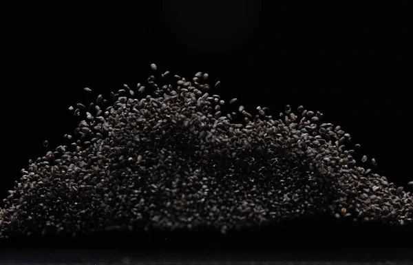 Black Sesame seeds flying explosion, black grain wave floating. Abstract cloud fly splash in air. Sesame seed is material food.  Black background Isolated selective focus blur