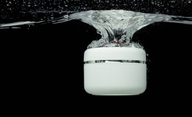 Kozmetik kabı hava kabarcığı ile berrak suya düşer. Temiz suya küçük bir kozmetik tedavi konteynırı düşüyor. Siyah arkaplan izole edilmiş dondurucu element