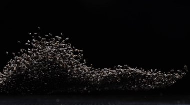 Kara susam tohumları uçuşan patlamalar, yüzen siyah tahıl dalgaları. Soyut bulut sineği havaya sıçrar. Susam tohumu maddi gıdadır. Siyah arkaplan izole seçili odak bulanıklığı