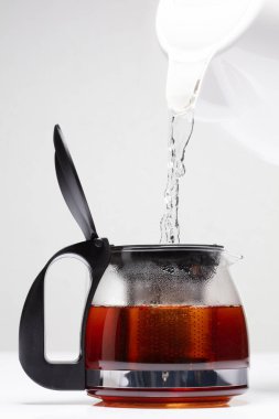 Tencere dibin kara seninki benden kara, seninki benden kara. Kahverengi sudan kurumuş yaprak çayını süzmek için şeffaf çaydanlık. Beyaz arkaplan izole edilmiş fırlatma dondurma hareketi