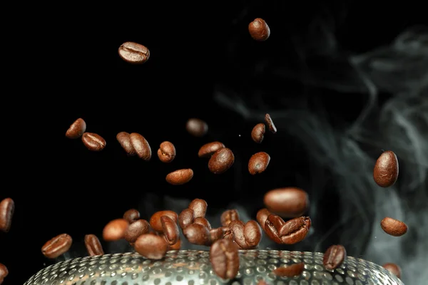 Roasted Coffee seeds with smoke. Beans Coffee roasted on pile and hot smoke raise up in line shape. Roasted coffee bean create scent aroma. Black background isolated