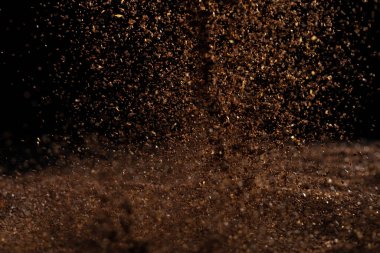 Ground Coffee roasted powder dust fly explosion, Coffee crushed ground float pouring. Roasted Coffee powder ground dust splash explosion in mid Air. Black background Isolated selective focus blur