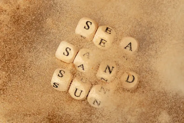 アルファベットの文字の文言 海砂の日 ビーズおもちゃ爆発の上空を飛んで空気中の飛行 海砂サンワードアルファベット文字は休暇のための熱帯の島のビーチの砂を示しています トップ表示アクション ロイヤリティフリーのストック画像