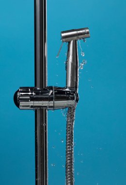 Su tıkandığı sırada banyodaki su borularından bidet duşu başlığı suyu sızıyor. Mavi banyo arka planı izole edildi. Krom, paslanmaz çelik bide duş başlığından su sızdırıyor.