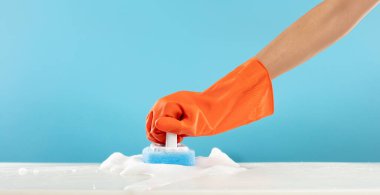 Turuncu kauçuk eldiveni tut temizlik fırçası süngeri temizle köpük köpüğü havayı mavi arka plana sıçrat, zemini temizle köpük köpüğü banyoya sıçra.