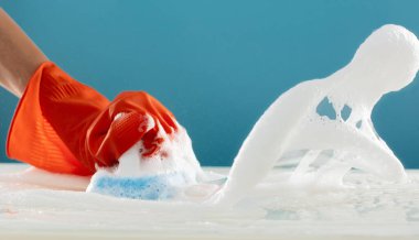 Turuncu kauçuk eldiveni tut temizlik fırçası süngeri temizle köpük köpüğü havayı mavi arka plana sıçrat, zemini temizle köpük köpüğü banyoya sıçra.