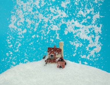 Mavi gökyüzü arka planında kar yağışı evi izole edildi. Kış fırtınası, iklim değişikliğinin yarattığı çığ gibi eve düşüyor.
