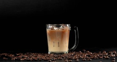 Bardakta buzlu kahve ve kızarmış fasulye düşüyor. Siyah arkaplan izole eleman. Birçok kahve çekirdeği aromalı buzlu sütün üzerine düşer.