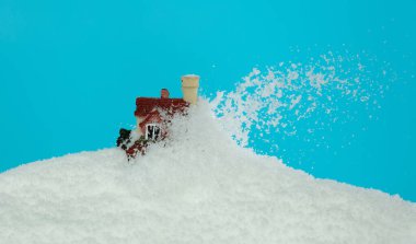 Mavi gökyüzü arka planında kar yağışı evi izole edildi. Kış fırtınası, iklim değişikliğinin yarattığı çığ gibi eve düşüyor.