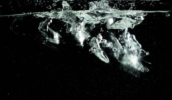 Falling ice tube pieces with water splashing in midair on a transparent, isolated black background. Ice tubes drop into water with air bubbles scatter splashing