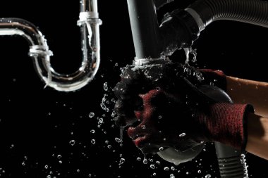 Tesisatçı mutfak lavabosunun altındaki su boşaltma borusunda gevşek fındığı sıkmak için anahtar kullanmış. Eldiven, duvarın arkasındaki sızıntıya ulaşmak ve su sızıntısını durdurmak için özel bir alet.