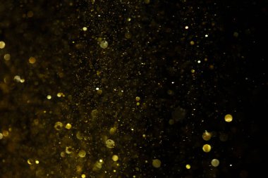 Altın parıltı tozu fotoğrafı soyut bokeh şenlik atmosferi yaratıyor. Altın parıltılı parçacık elementi Bokeh kumu lüks arka planı aydınlatır, ışıltılı duvar kağıdı