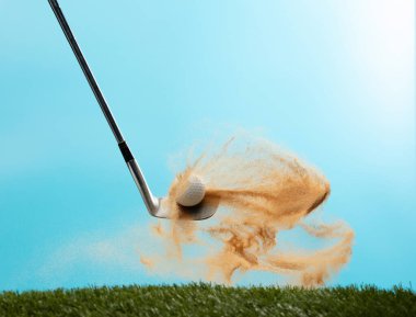 Golf topu Tee off 'tan patladı. Golf sopası ile topa vuran golfçü yeşilde kum patlaması yaptı. Golf sopası yeşil golf sahasında kum saçmasıyla topa vurdu. Mavi Gökyüzü arkaplanı izole edildi