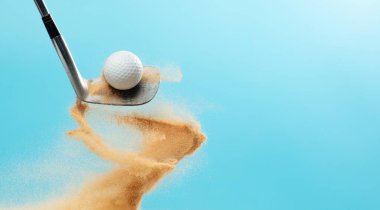 Golf topu Tee off 'tan patladı. Golf sopası ile topa vuran golfçü yeşilde kum patlaması yaptı. Golf sopası yeşil golf sahasında kum saçmasıyla topa vurdu. Mavi Gökyüzü arkaplanı izole edildi
