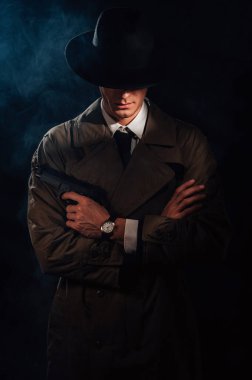 Silhouette of a male detective in a coat and hat with a gun in his hands. A book drama noir portrait in the style of detectives of the 1950s